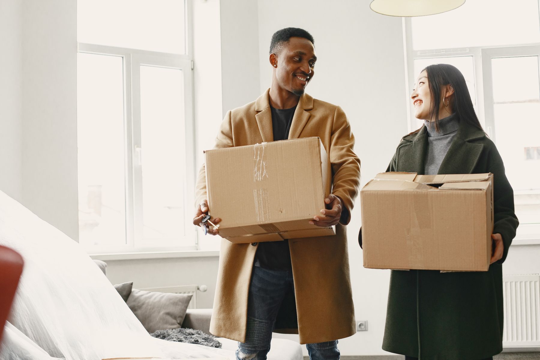 Pareja sonriente cargando cajas de cartón en su nuevo hogar luminoso